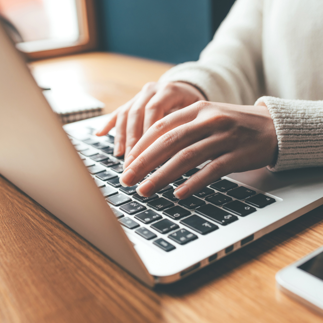 Hands typing on a laptop keyboard on a wooden desk, representing the flexibility of tailoring marketing services to fit your unique goals.