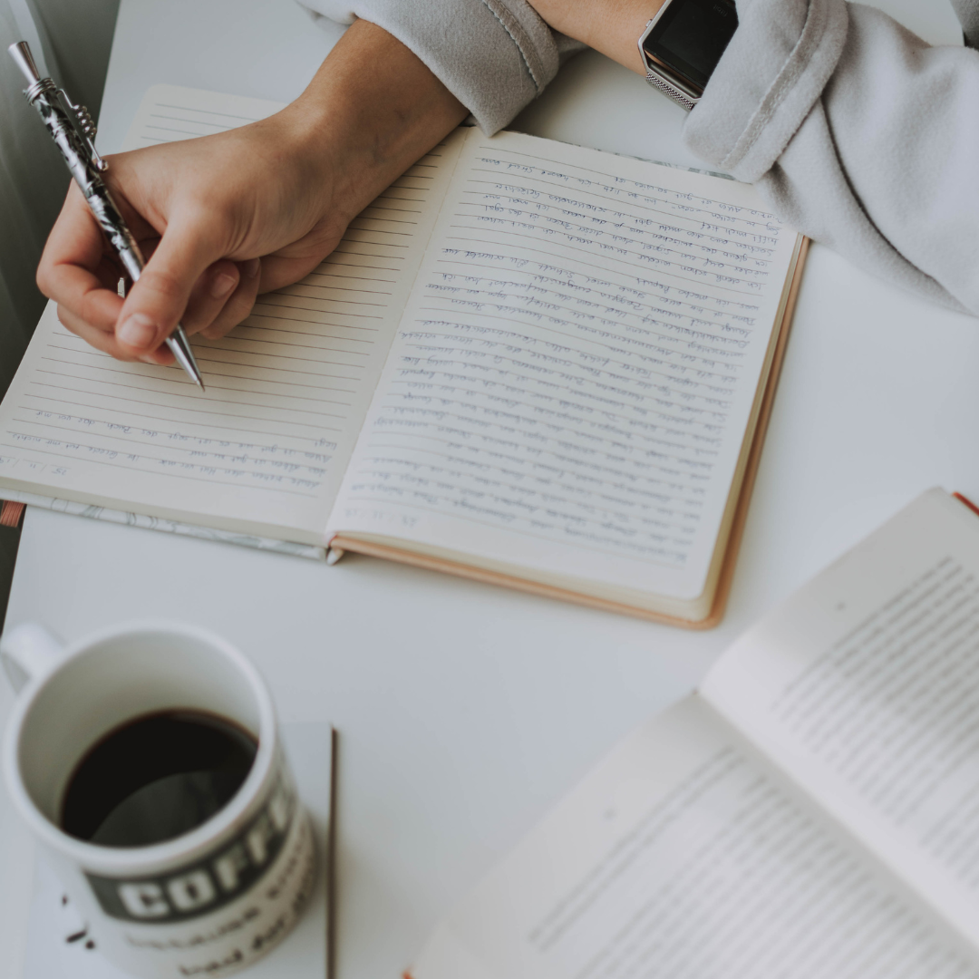 A person writing in a notebook, surrounded by an open book and a coffee mug, illustrating the hands-on and personalized approach of the Choose Your Own Adventure package.