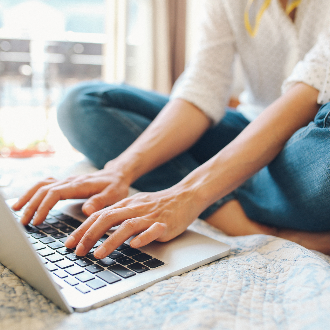 A person sitting cross-legged on a bed, typing on a laptop in a relaxed and comfortable setting, representing the comprehensive and approachable support offered in the Epic Experience package.