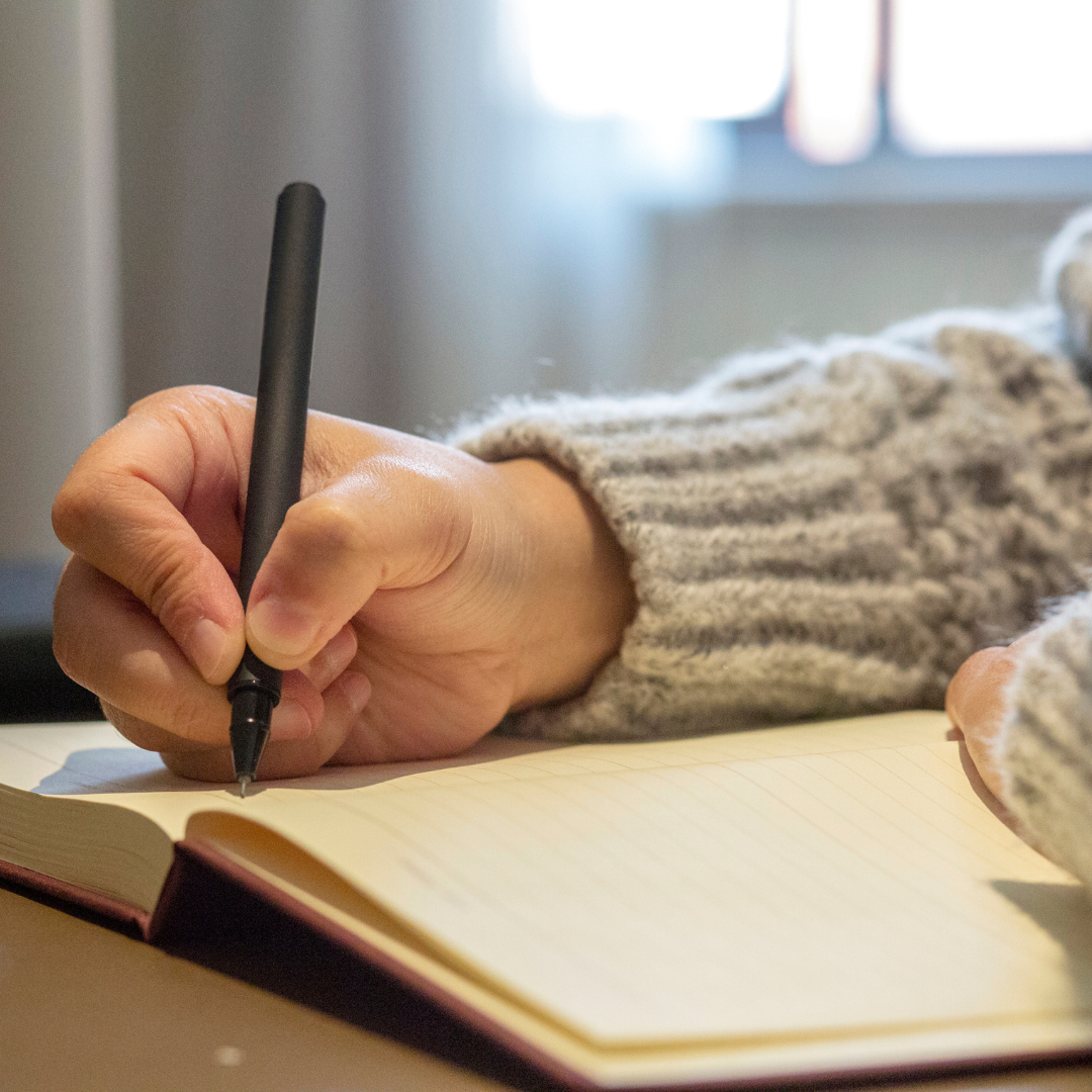 Close-up of a person writing in a journal while wearing a cozy sweater, representing the thoughtful, tailored approach of the Novel Narrative package for authors preparing to expand their reach.