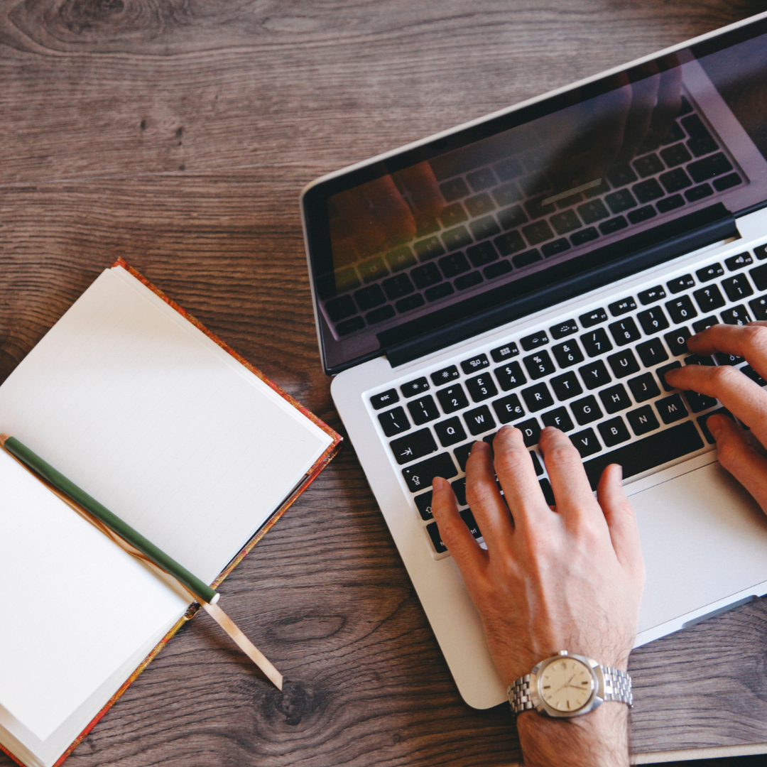 Overhead view of a person typing on a laptop beside an open notebook and pencil on a wooden table, representing the hands-on and practical learning approach of the Storyline Success package.